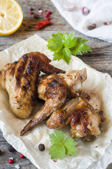 Chicken wings baked on grill with fresh herbs, lemon on wooden background.