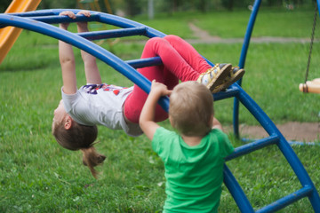 brother and sister climb and hang on a metal ladder in the form of an arc in the playground.