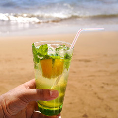 Cold mojito drink on the beach sand. Summer vacation concept image.