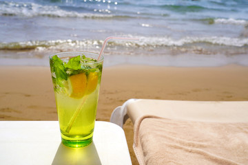 Cold mojito drink and sunbed on the beach sand. Summer vacation concept image.