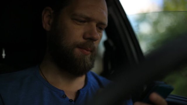 a bearded man sitting behind the wheel of a car and talking on the phone.