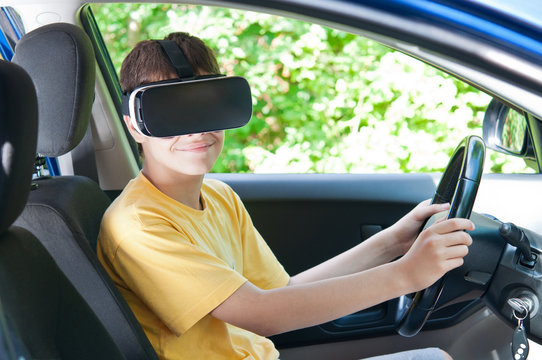 A teenager in virtual reality glasses, driving a car.