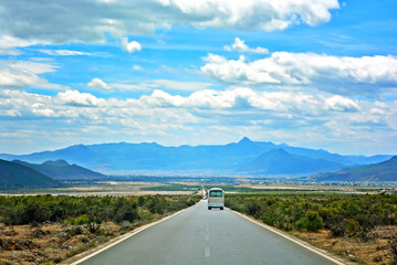 Road in the middle of natural mountain landscape with a van and car on the road with blue sky...