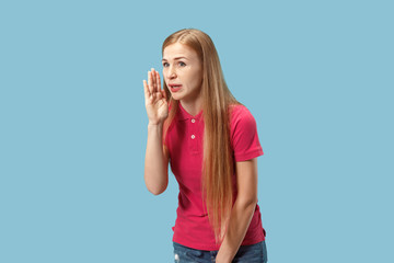 The young woman whispering a secret behind her hand over blue background