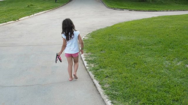 The child goes barefoot. A little girl walks in the park barefoot.