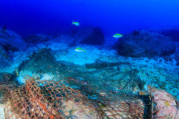 Discarded fishing net (Ghost net) on the sea floor next to a tropical coral reef