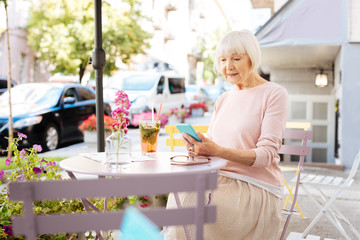 Internet connection. Concentrated senior woman using phone and sitting at table