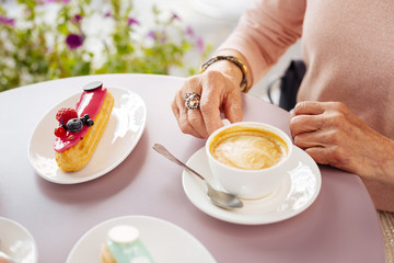Enjoy coffee. Close up of porcelain fragile cup filled with coffee and eclairs placing on table