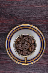 An old cup full of coffee beans with its plate