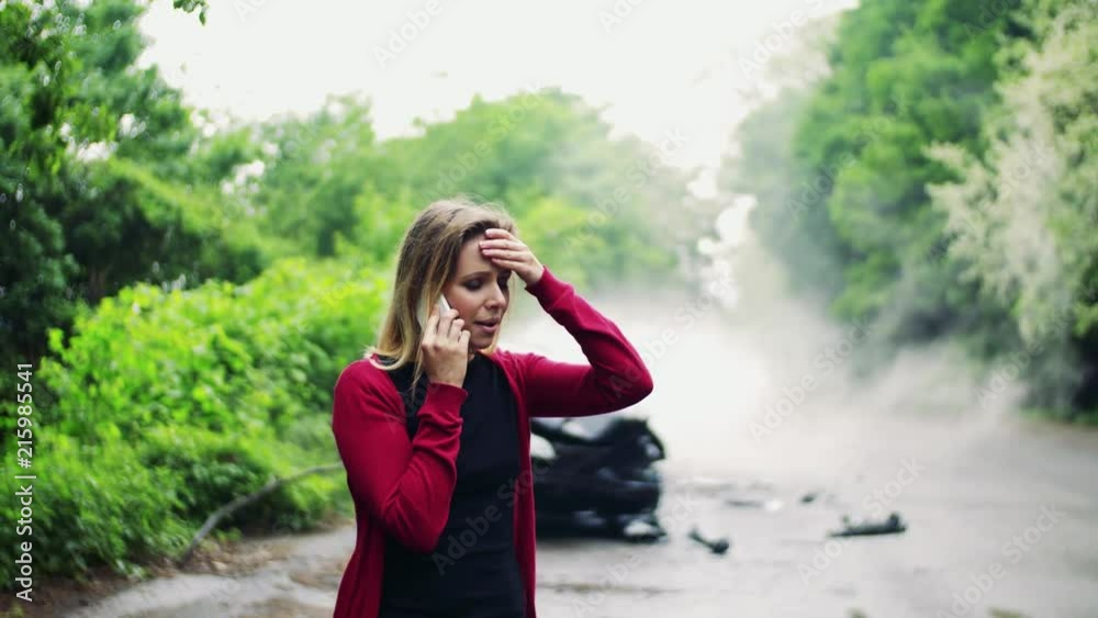 Wall mural Young woman making a phone call after a car accident, smoke in the background.