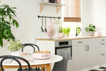 Real photo of sponge cake on a white, round dining table in open space kitchen interior with white cupboards