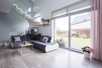 Foto auf Acrylglas Natural light coming through big glass door to a monochromatic, open space living room interior with a modern sofa on hardwood floor © Photographee.eu