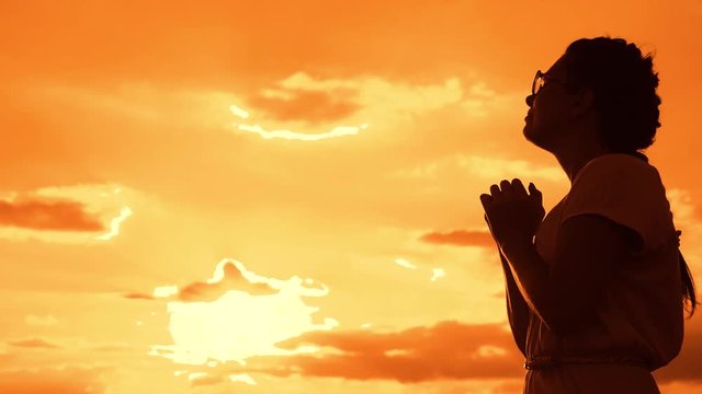 the girl prays. Girl folded her hands in prayer silhouette at sunset. slow motion video. Girl folded her hands in prayer pray to God. girl lifestyle praying asks forgiveness for sins of repentance