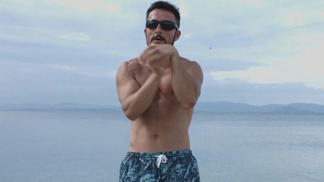 Man Wearing Sunglassess Stretching Arms in a Warm Exercise Along the Sea Coast