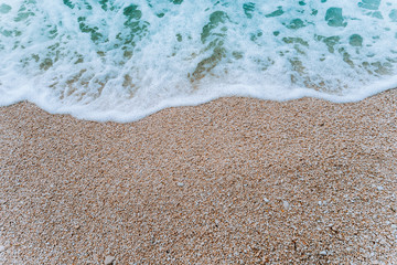 Rolling soft foam wave of blue turquoise sea water on pebble beach. Background. Top view