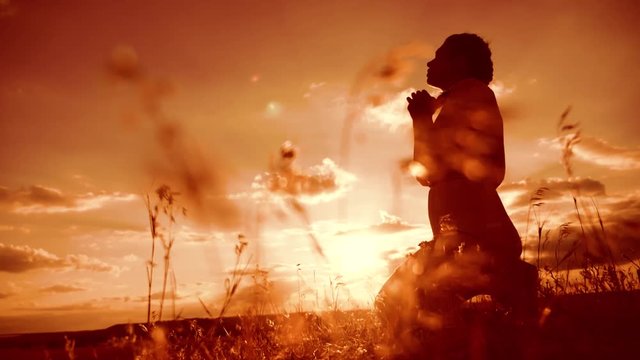 woman praying on her knees. Girl folded her hands in prayer silhouette at sunset. slow motion video. Girl folded her hands in prayer pray to God. the girl praying asks forgiveness for sins of