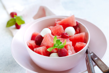 Watermelon salad with raspberry and mozzarella in pink bowl on white table