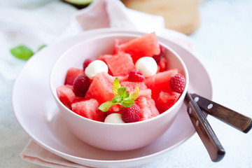 Watermelon salad with raspberry and mozzarella in pink bowl on white table