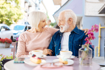 Great mood. Enthusiastic senior couple sitting at cafe and staring at each other