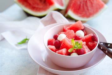 Watermelon salad with raspberry and mozzarella in pink bowl on white table