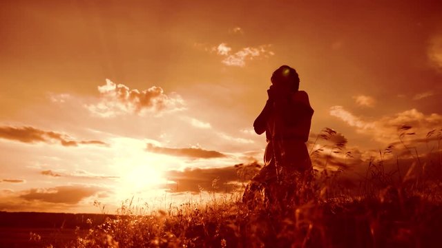 Girl folded her hands in prayer silhouette at sunset. woman praying on her knees. slow motion video. Girl folded lifestyle her hands in prayer pray to God. the girl praying asks forgiveness for sins