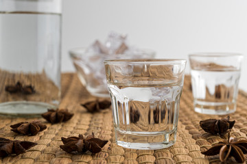 Glasses and bottle of traditional drink Ouzo or Raki with anise star seeds on natural matting