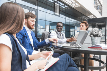 Group of happy diverse male and female business people team in formal gathered around laptop computer in bright office against the background of a glass building
