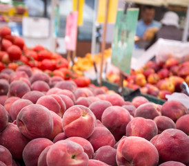 Farmers market fruit stall with peaches, tomatoes and nectarines.  People out of focus in the background.  Many colorful signs.