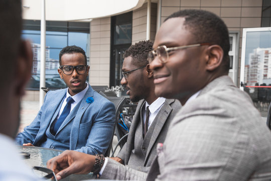 Group of happy diverse male business afro - american people team in formal gathered around laptop computer in bright office against the background of a glass building