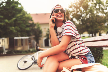 Smiling girl with sunglasses sitting on a bench in the summer using smart phone