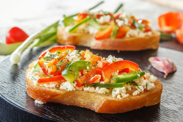 Bruschetta with red sweet pepper and goat cheese on a black plate. Close-up