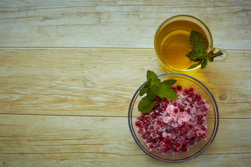 a transparent Cup with green tea and a leaf of mint stands next to the plate, in which lies a red currant, sprinkled with sugar on a wooden table.