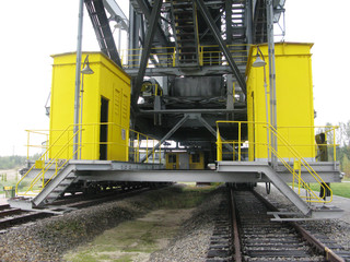 yellow steel cabins on a platform, steel ladders, traverses, beams, steel stairs and tracks, working place a sparse landscape with trees on horizon, industrial building site