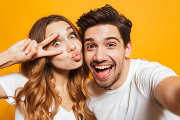 Portrait of caucasian man and woman taking selfie photo and showing peace sign, isolated over...