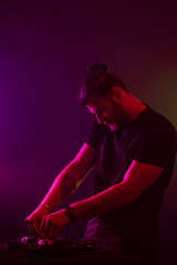 Attractive young DJ playing on turntables with color light effects