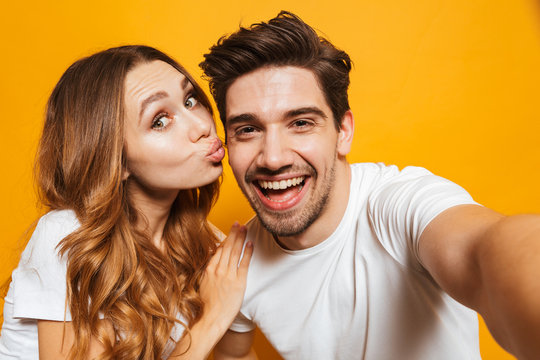 Portrait of caucasian attractive couple man and woman taking selfie photo together, isolated over yellow background