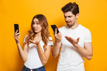 Confused young couple looking at mobile phones