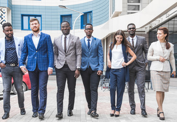 Obraz premium Successful company with happy workers. Men and women in business suits stand with their arms crossed against the background of skyscrapers