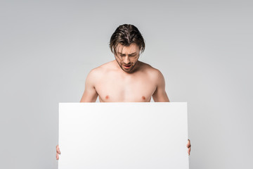 portrait of handsome shirtless man looking at blank banner in hands isolated on grey