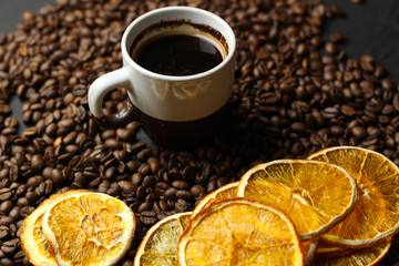 A cup of coffee, snacks of dried oranges and coffee beans on a dark background. Delicious coffee of the best varieties