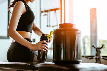 Relaxing after training.beautiful young woman looking away while sitting  at gym.young female at gym taking a break from workout.woman brewing protein shake. - obrazy, fototapety, plakaty