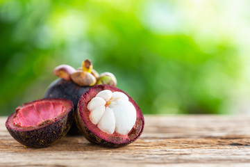Obraz na płótnie Canvas Purple mangosteen fruit on wooden table background with green blur light space background