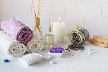 Fototapeta na wymiar Wellness setting. Purple sea salt, towel, massage oil , lavender flowers and candle on white textured background. Space for text