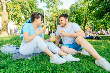 couple sitting on green grass eating burgers drinking smoothie