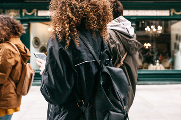 A tourist girl with curly hair with a backpack or a student walking down the street and using a mobile phone or cell phone.