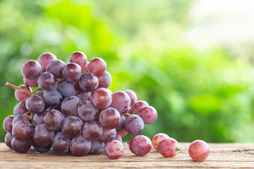 Bunch of ripe red grapes on wooden table with green space blur