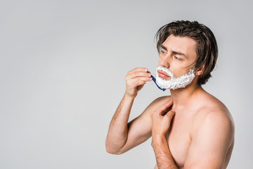 side view of shirtless man with foam on face shaving beard isolated on grey