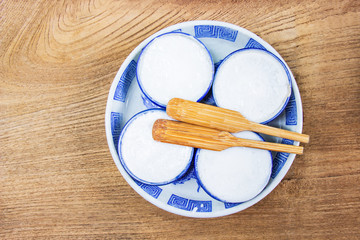 Thai Coconut Milk Custard is a thai dessert made from rice flour, coconut milk and sugar put the small ceramic cups place are on a wooden floor. Khanom Thuai