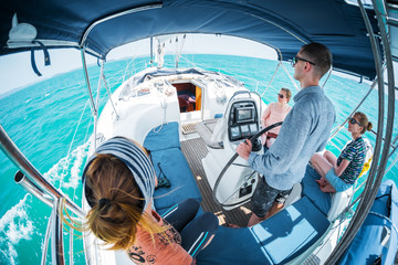 Young captain steers sailing boat in a tropical sea with three young ladies on board