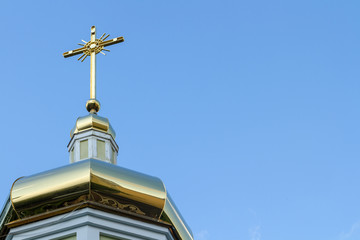 Fototapeta na wymiar Cross on the golden dome of the Orthodox church against the blue sky. The cross is a symbol of Orthodoxy. The Golden Cross is a symbol of the Church of Jesus Christ.